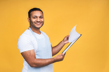 Cooking, culinary and people concept - african american indian male chef with clipboard isolated over yellow background.