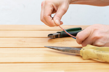 Hands with pliers and pliers removing the protection from an electrical cable for repair