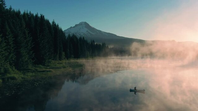 Aerial: Canoe rowing on Trillium Lake, mist, pine forest and Mt Hood at sunrise, Oregon, USA