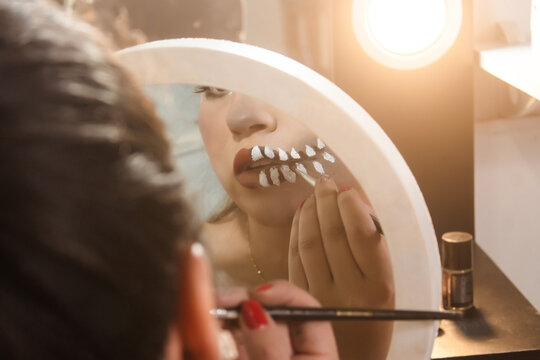 Beautiful girl doing skull teeth makeup on her lips for Halloween in her bedroom.