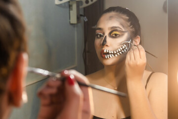 Girl concentrating on making up an artistic skull for Halloween in her room.