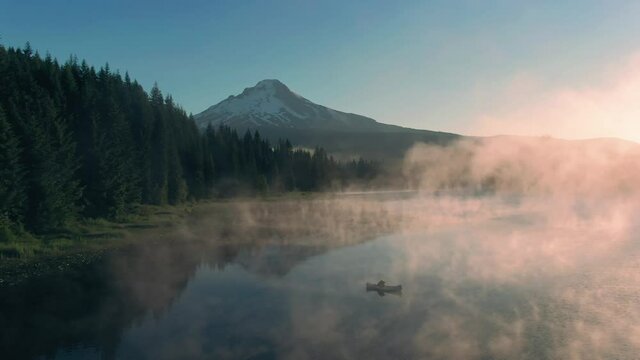 Aerial: Canoe rowing on Trillium Lake, mist, pine forest and Mt Hood at sunrise, Oregon, USA