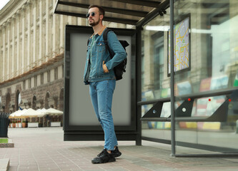 Young man with backpack waiting for public transport at bus stop