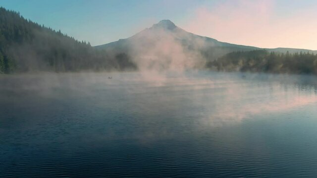 Aerial: Canoe rowing on Trillium Lake, mist, pine forest and Mt Hood at sunrise, Oregon, USA
