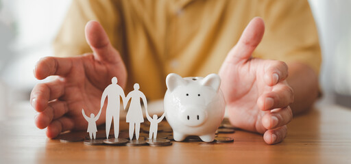 Businessman take a position to protect on the piggybank and paper family in hand, donation, saving, charity, family finance plan concept, fundraising, superannuation, financial crisis concept