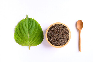 Perilla seeds in a wooden bowl with spoon and perilla leaf on white background, Healthy herbal seed ingredients in Asian food, Top view