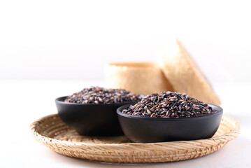 Purple glutinous rice grain in a black bowl and bamboo container on white background, Thai rice
