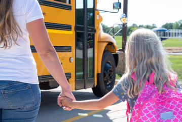 Little girl holding her mom's hand waiting to get on a school bus © Kristen