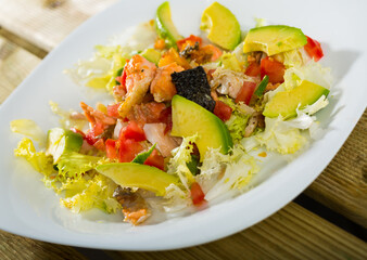 Healthy salad with chopped fried salmon, avocado, fresh tomatoes and Chinese cabbage on white plate