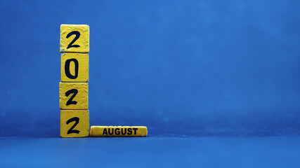 Wooden block calendar showing August 2022. Isolated on blue background
