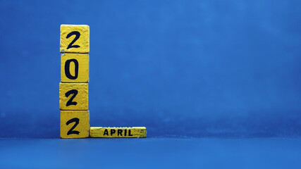 Wooden block calendar showing April 2022. Isolated on blue background