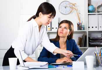 Two businesswomen sitting at desk and working together at office