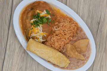 Overhead view of hearty plate of chili relleno smothered in wet sauce served with rice and refried beans