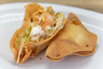 Hearty side order of crispy fried potato taco loaded with meat and vegetables inside a hard shell