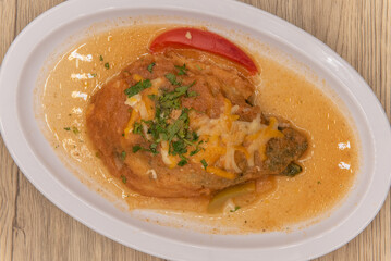Overhead view of hearty appetizer of chili relleno smothered in wet sauce with a slice of pepper on the plate