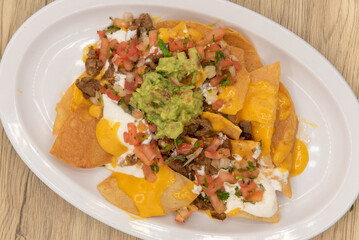 Overhead view of hearty plate of nachos smothered with melted cheese, pico de gallo, and sour cream to serve as a meal