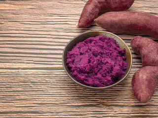 Pile of purple yams and mashed potatoes on dish placed on wooden table with copy space for text. Purple sweet potatoes. Top view. Vegan fruit and healthy fruits concept