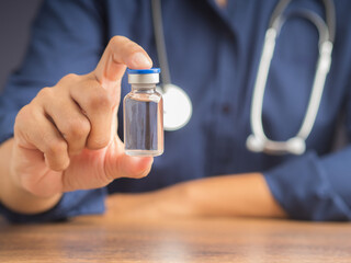A doctor is holding a vaccine bottle while sitting in the hospital. Vaccine for prevention and...