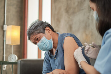 Obraz premium An Asian female doctor is vaccinating an elderly man who wears a mask to prevent illness from the virus infection. It is home healthcare by professionals to treat sick people who are retired.