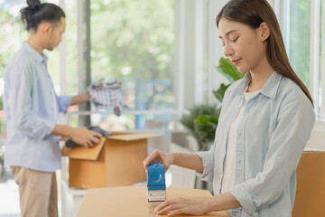 Fototapeta premium Happy couple asian young woman, man.packing stuff clothes, give second hand for donate, check list object in cardboard box. Moving, preparing in new home, apartment relocation. Mortgage, real estate.