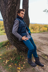 Tall handsome man standing near the tree in autumn forest