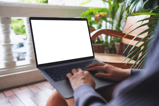 Mockup image of a woman using and working on laptop computer with blank white desktop screen while sitting on balcony at home