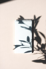 Mockup blank white spiral notebook. Stationery still life with shadows from olive branch, view from above.