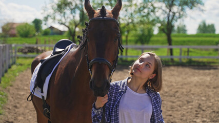 Fototapeta premium a young beautiful brunette looks at the horse next to her on the ranch. High-quality photo