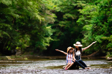 渓流の岩に座って手を上げる母と娘