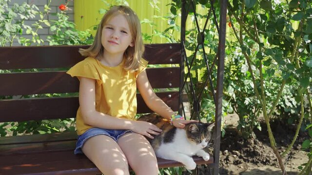 little girl strokes stray cat sitting on a bench with beautiful landscaping