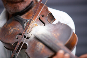 Close up partial photo of an old musician holding violin in his hand and playing the classical melody being outdoors.