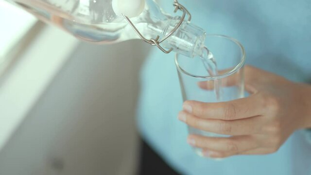 Closeup woman hands pouring water into glass from bottle. Slow motion.