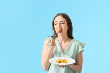 Beautiful young woman eating tasty ravioli on color background