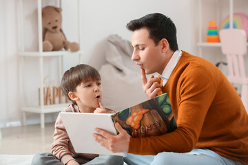 Speech therapist with little boy reading book in office