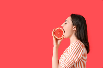 Beautiful young woman eating grapefruit on color background