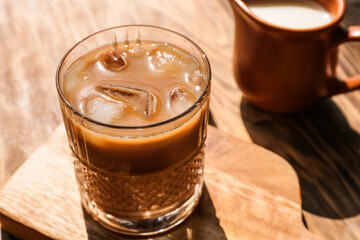 Wooden board with glass of tasty iced coffee on table