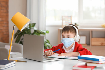 Fototapeta na wymiar Little schoolboy in medical mask studying online at home
