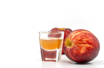 Small Shot Glass of organic Apple Cider Vinegar with the mother, two red apples is aside of the glass, image on white background.