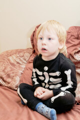 Fototapeta premium A child in a skeleton costume sits on the couch with an emotion on his face