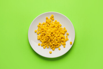 Plate with corn kernels on color background