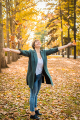 middle-aged woman walks, throwing orange leaves in the autumn park. active lifestyle, happy pension