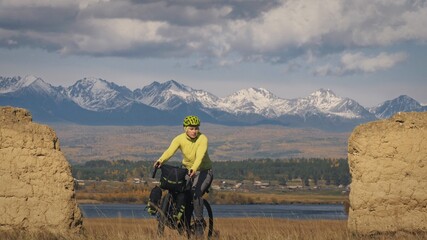 Fototapeta premium The man travel on mixed terrain cycle touring with bikepacking. The traveler journey with bicycle bags. Sport bikepacking, bike, sportswear in green black colors. Mountain snow capped, stone arch.