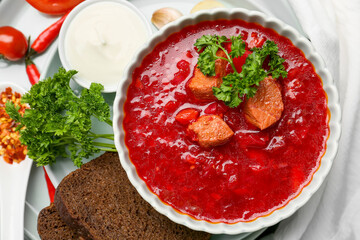 Bowl of tasty borscht with sour cream and bread on light fabric background