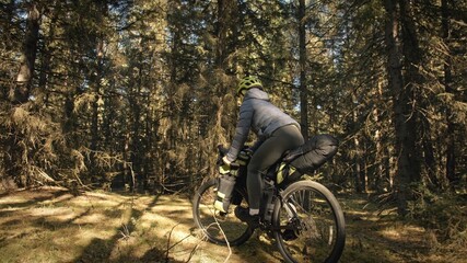 Fototapeta premium The woman travel on mixed terrain cycle touring with bike bikepacking outdoor. The traveler journey with bicycle bags. Stylish bikepacking, bike, sportswear in green black colors. Magic forest park.