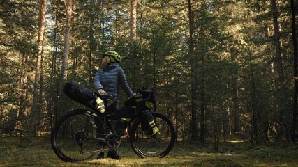 Fototapeta premium The woman travel on mixed terrain cycle touring with bike bikepacking outdoor. The traveler journey with bicycle bags. Stylish bikepacking, bike, sportswear in green black colors. Magic forest park.