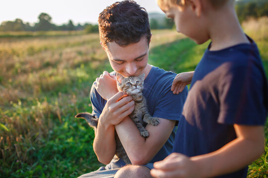 Young guy found and picked up little stripped kitten during walking in the field and going to home it, homeless domestic animals care, concept of volunteering and animal rescue