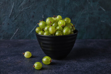Bowls with fresh ripe gooseberry on dark background