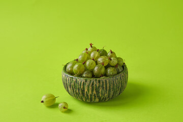 Bowl with fresh ripe gooseberry on color background