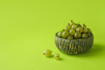Bowl with fresh ripe gooseberry on color background