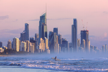 Surfers Paradise cityscape, with surfer going into the ocean - obrazy, fototapety, plakaty